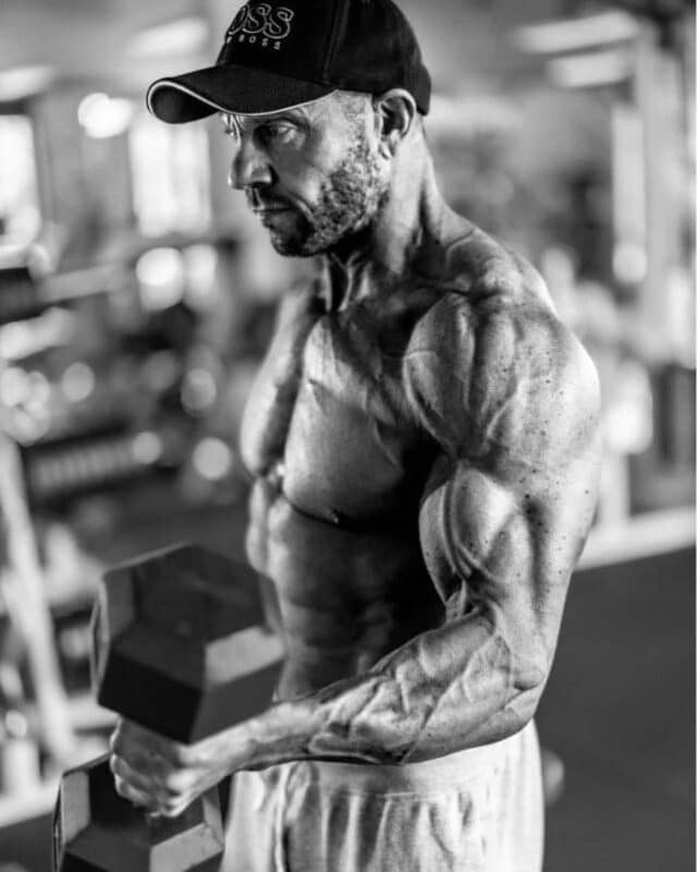 WOODIE-ONLINE-FITNESS-COACH-TOPLESS-POSING-IN-GYM-DUMBELL